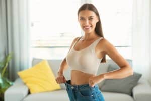 Smiling woman wearing jeans that fit her too big to show how much weight she has lost.