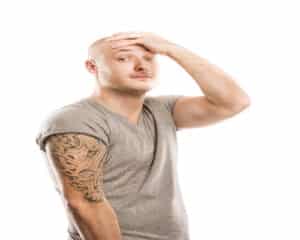 Man with a large tattoo on his arm holding his head in regret, in need of PicoSure tattoo removal