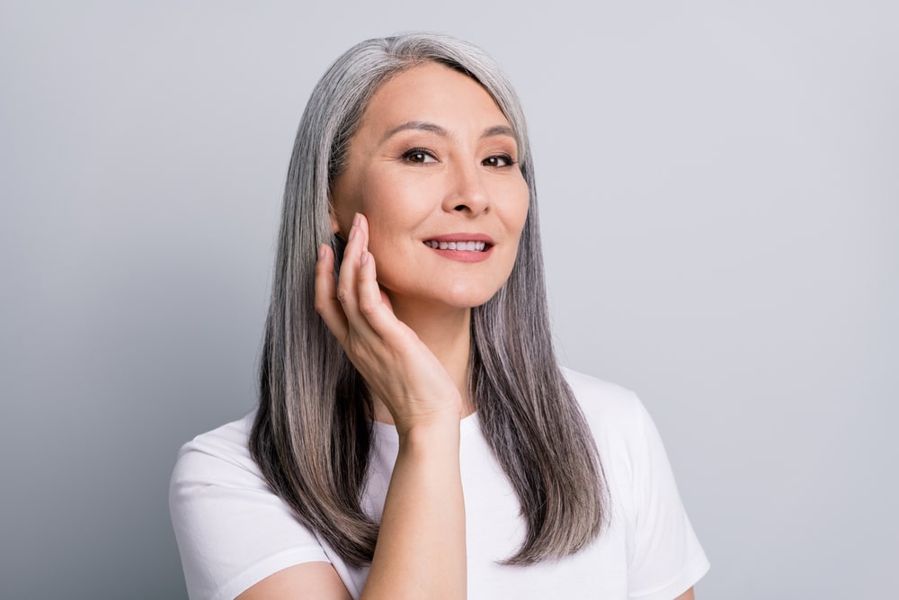 Older woman smiling happily and touching the smooth skin on her face after getting DAXXIFY injections.