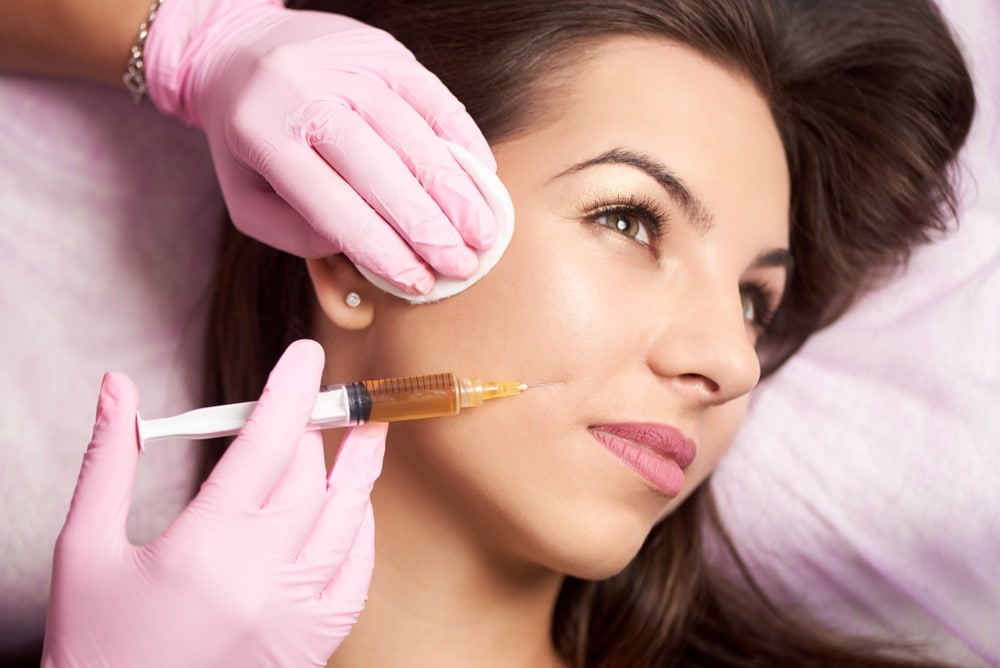 Close-up of a woman's face from the side, getting dermal filler injections from a provider to improve cheek volume.